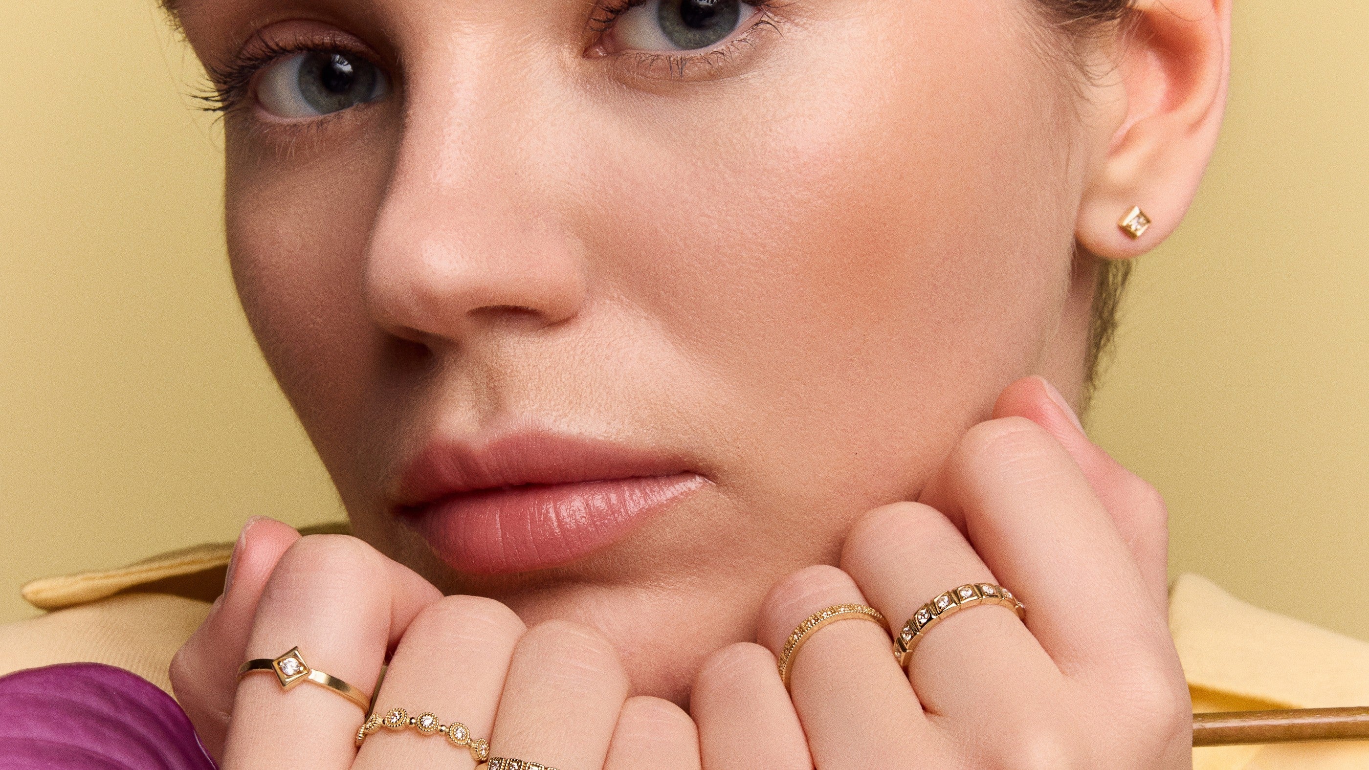 woman resting her chin on stacked gold rings against a warm yellow background