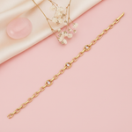gold open-link chain bracelet with framed baguette stones laid diagonally on pink background with dried flowers