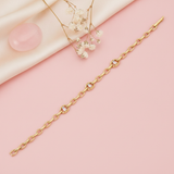 gold open-link chain bracelet with framed baguette stones laid diagonally on pink background with dried flowers