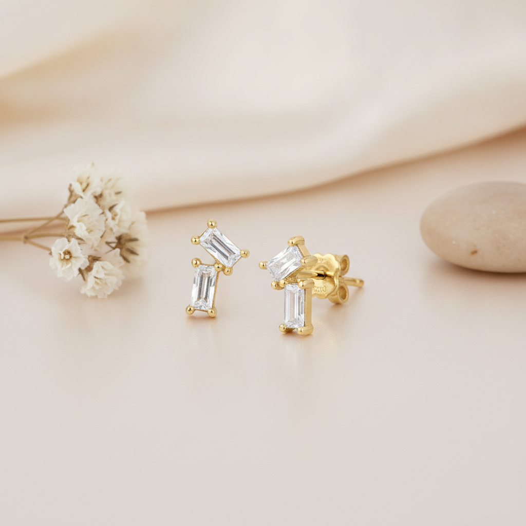 gold stud earrings with two angled baguette stones arranged in an L-shape, close up on cream background with dried flowers