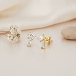 gold stud earrings with two angled baguette stones arranged in an L-shape, close up on cream background with dried flowers