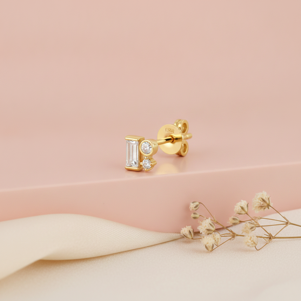 gold stud earrings with a baguette stone and two round accent stones, blurred pink background with dried flowers and moonstone
