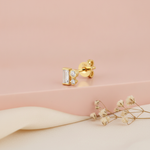 gold stud earrings with a baguette stone and two round accent stones, blurred pink background with dried flowers and moonstone