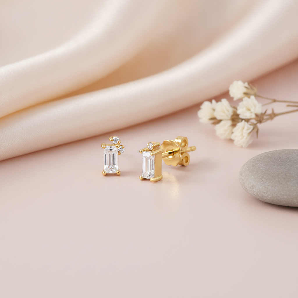 gold stud earrings with a vertical baguette stone and a cluster of small round accent stones, close up on cream background