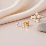 gold stud earrings with a vertical baguette stone and a cluster of small round accent stones, close up on cream background