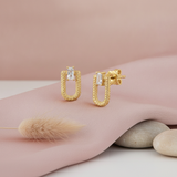 gold textured open-link stud earrings with a baguette stone, on pink satin with dried bunny tail grass and pebbles