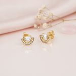 gold stud earrings with a pave crescent arc topped by a horizontal baguette stone, on pink satin with dried flowers and a rose quartz stone