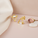 gold open triangle stud earrings with a horizontal baguette stone, on cream and pink background with a dried rose and pebbles
