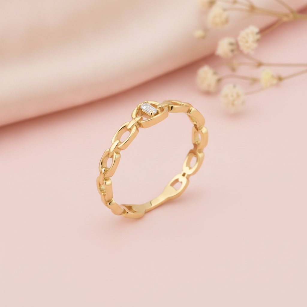 gold chain-link ring with a single baguette stone at center, on pink satin with dried flowers