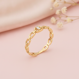 gold chain-link ring with a single baguette stone at center, on pink satin with dried flowers