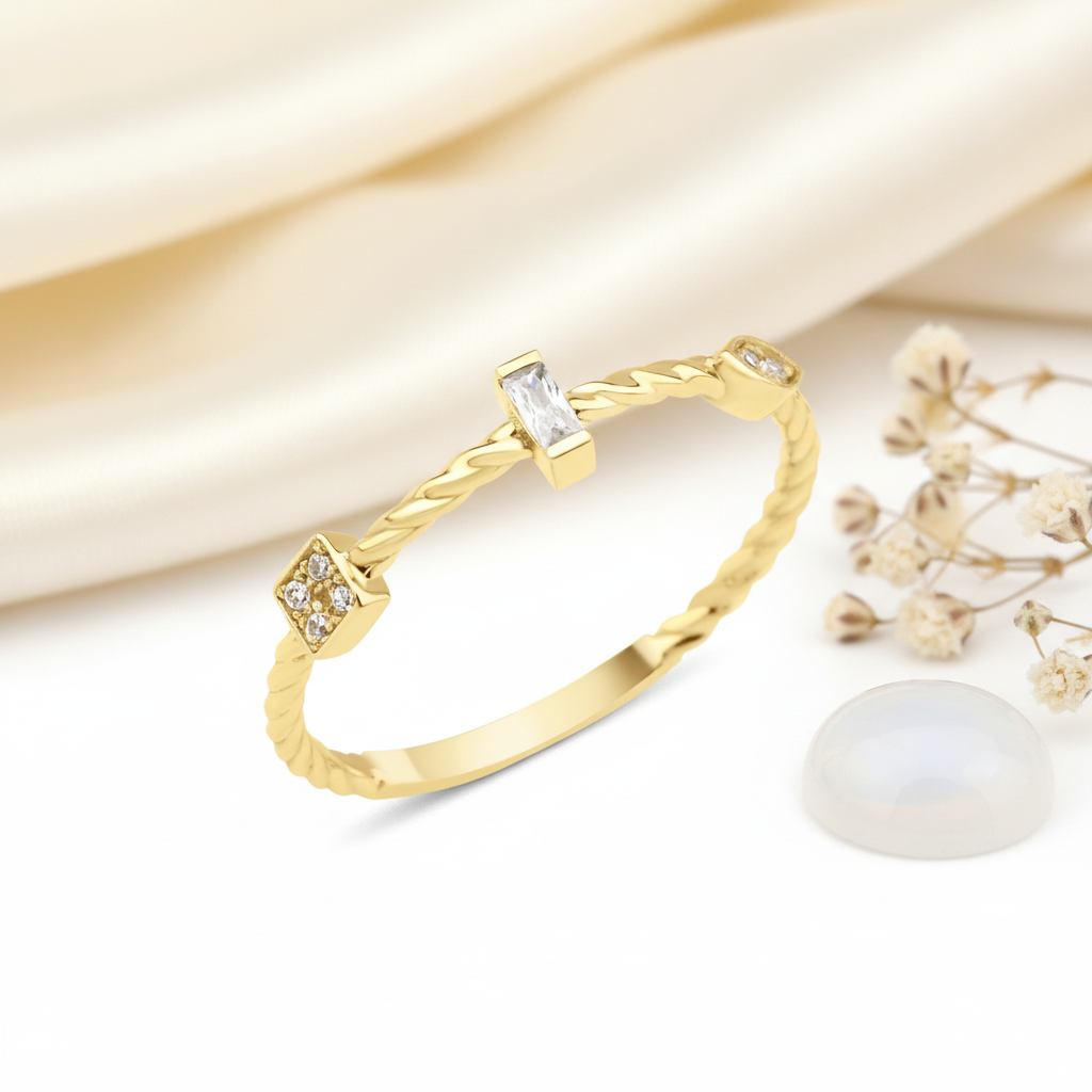 gold twisted ring with a baguette stone, square stone cluster, and bezel accent, on pink satin with dried flowers