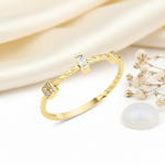 gold twisted ring with a baguette stone, square stone cluster, and bezel accent, on pink satin with dried flowers