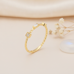 gold twisted band ring with a pave square, baguette stone, and round bezel accent, on pink satin with dried flowers