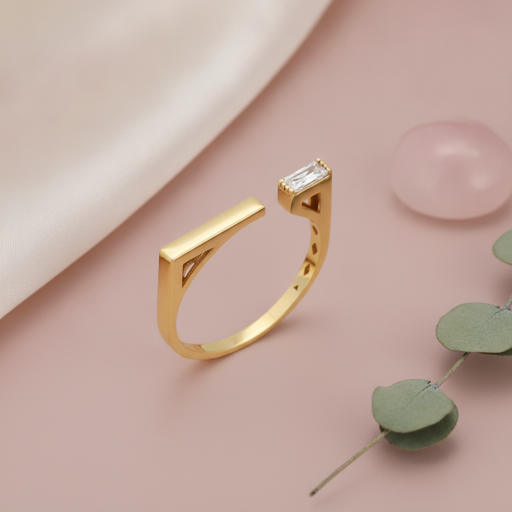 gold open ring with a polished bar on one side and a baguette stone on the other, on pink satin with a rose quartz stone and eucalyptus leaves