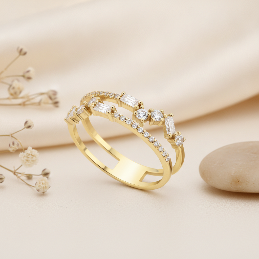 gold double-band ring with a stepped sequence of baguette and round pave stones, on pink satin with dried flowers and a pebble
