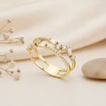 gold double-band ring with a stepped sequence of baguette and round pave stones, on pink satin with dried flowers and a pebble
