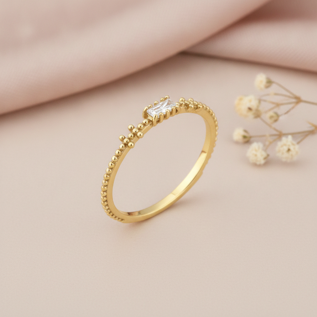 gold beaded texture ring with a horizontal baguette stone, on pink satin with dried flowers