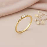 gold beaded texture ring with a horizontal baguette stone, on pink satin with dried flowers