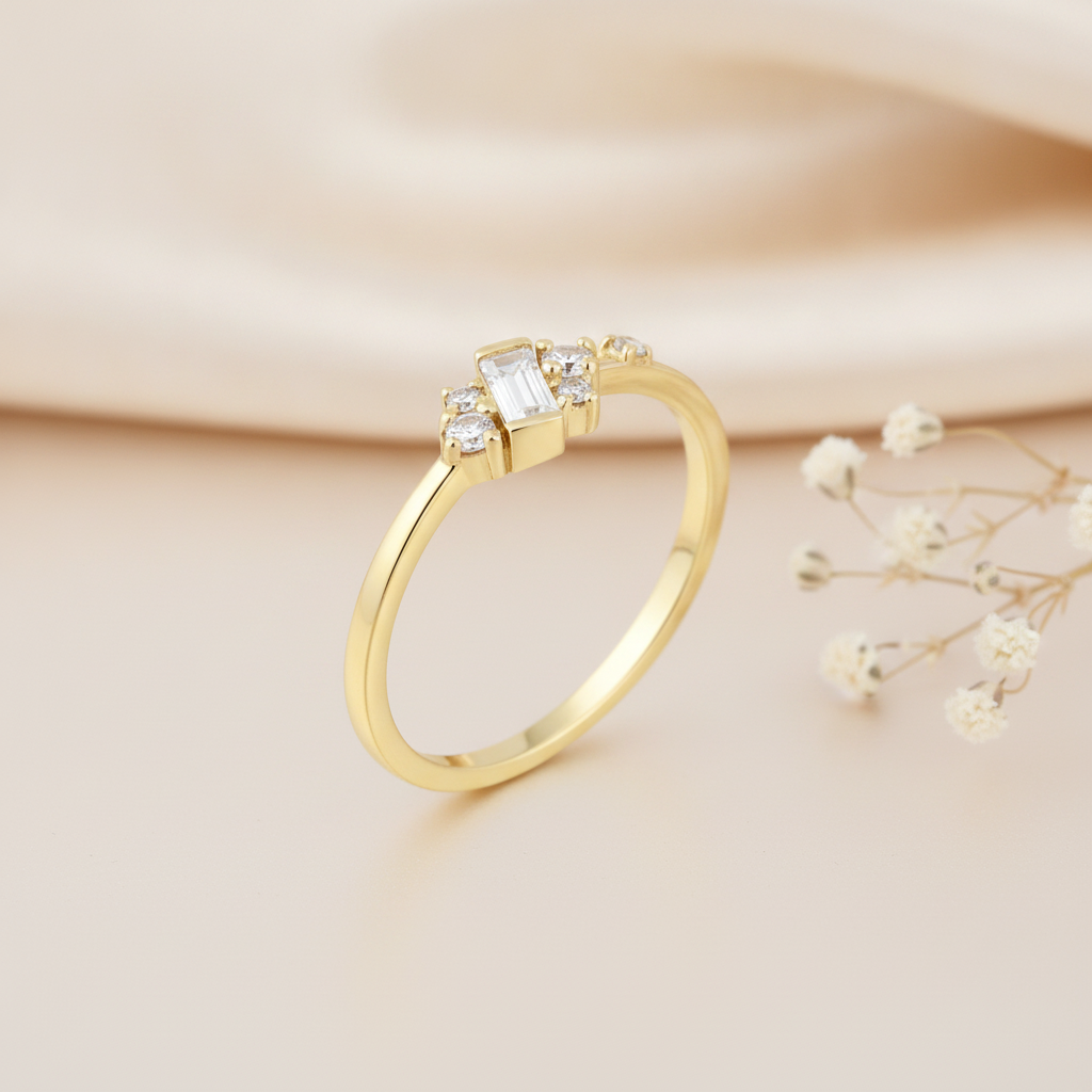 gold ring with a vertical baguette stone and a scattered cluster of round accent stones, on pink satin with dried flowers and a pebble