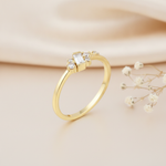 gold ring with a vertical baguette stone and a scattered cluster of round accent stones, on pink satin with dried flowers and a pebble
