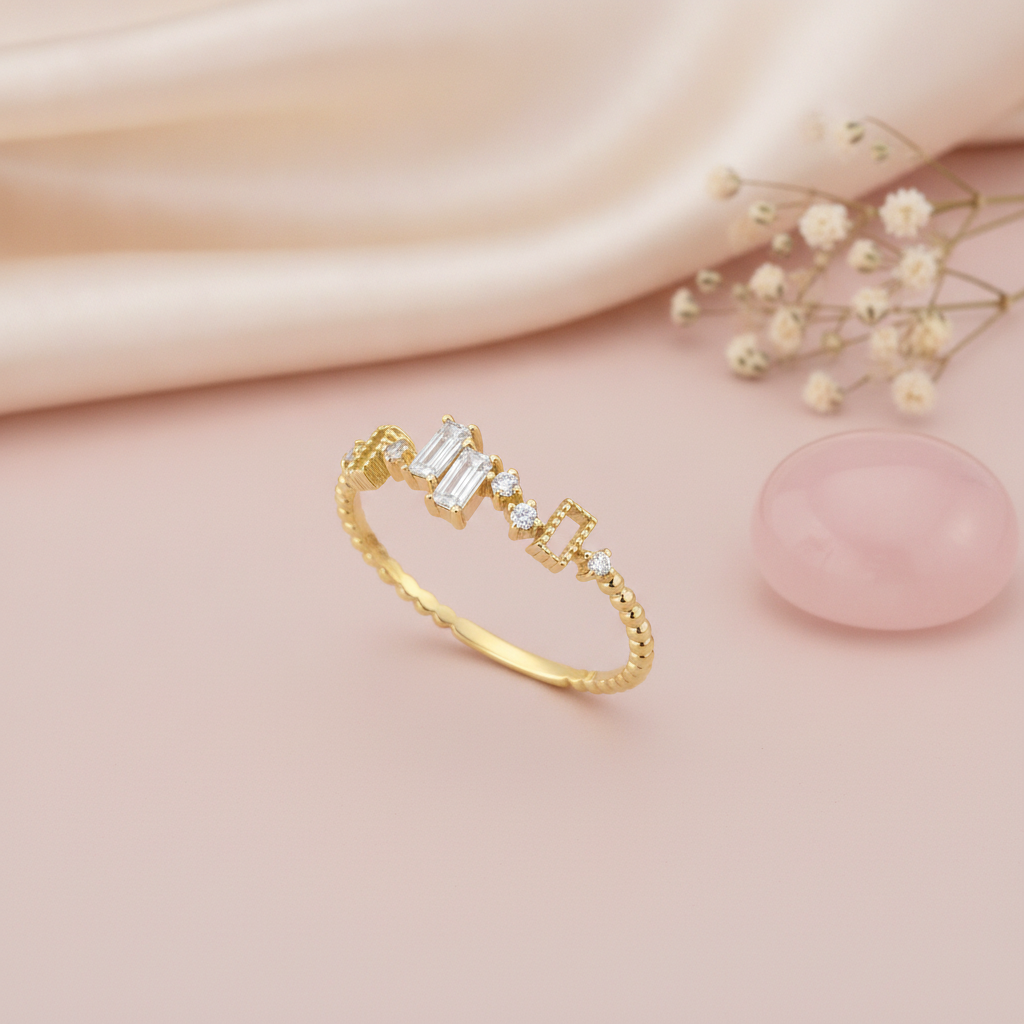 gold beaded band ring with baguette and round stones stepping across the top, on pink satin with dried flowers and a rose quartz stone