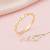 gold open ring with a baguette stone on one end and a smooth tapered tip on the other, on pink satin with dried baby's breath flowers