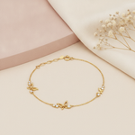 gold chain bracelet with three butterfly charm stations and accent stones, laid out on cream and pink background with dried flowers