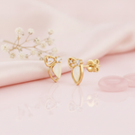 gold bow-and-wing stud earrings with a pale sculpted petal drop and two round accent stones, on pink satin with rose quartz discs