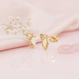 gold bow-and-wing stud earrings with a pale sculpted petal drop and two round accent stones, on pink satin with rose quartz discs
