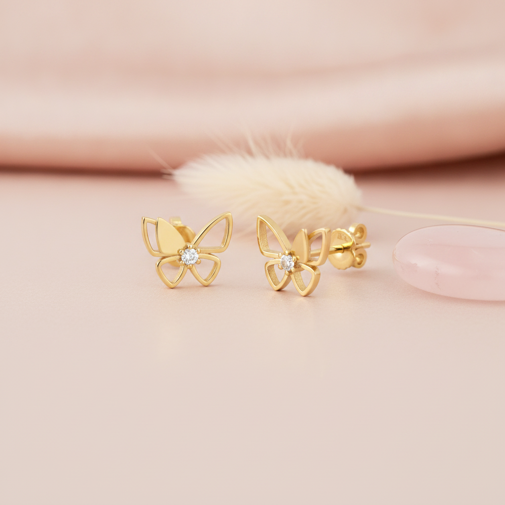 gold open-wing butterfly stud earrings with a round center stone, on cream background with flowers and pebbles