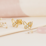 gold openwork butterfly stud earrings with clusters of pave stones, on pink and cream background with dried flowers and a rose quartz stone
