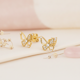 gold openwork butterfly stud earrings with clusters of pave stones, on pink and cream background with dried flowers and a rose quartz stone