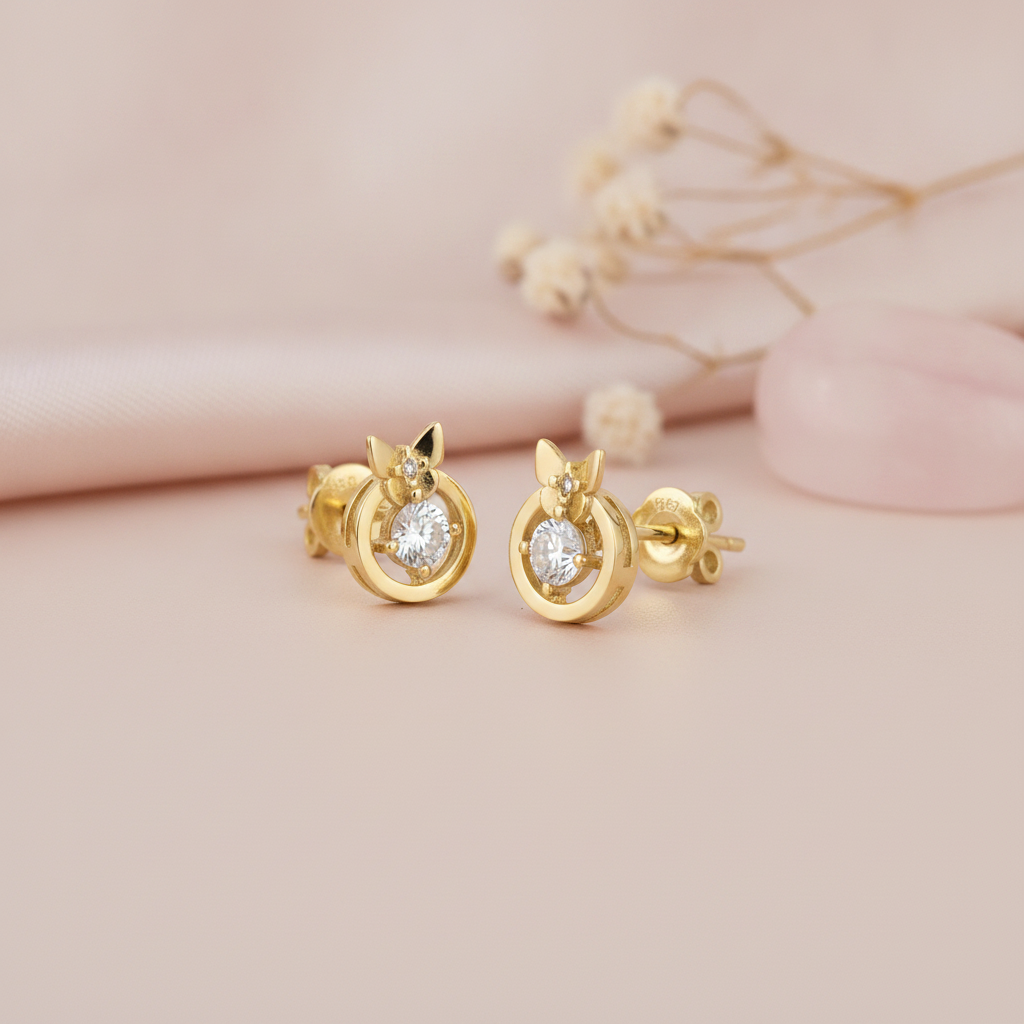 gold circular stud earrings topped with a small butterfly and a round center stone, on blush background with dried flowers