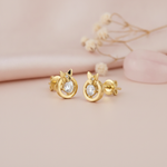 gold circular stud earrings topped with a small butterfly and a round center stone, on blush background with dried flowers