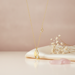 gold butterfly wing pendant necklace with clear stones displayed on cream fabric with rose quartz stones and dried flowers