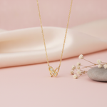 gold openwork butterfly pendant necklace with clear pave stones on pink satin with dried flowers and a smooth stone