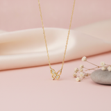 gold openwork butterfly pendant necklace with clear pave stones on pink satin with dried flowers and a smooth stone