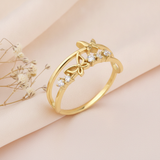 gold double-band ring with two butterfly motifs and clear stones displayed on blush satin fabric with dried flowers