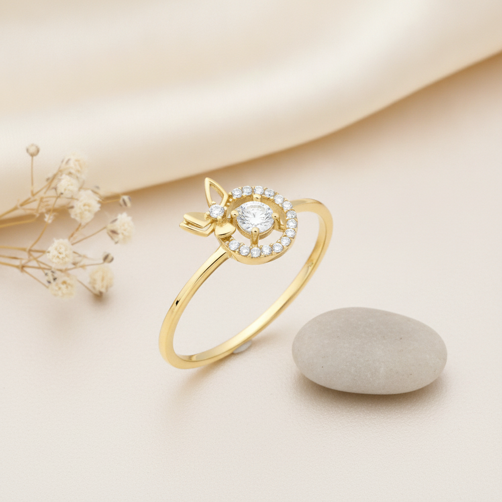 gold ring with a pave stone halo and side butterfly motif displayed on cream fabric with dried flowers and a smooth gray stone