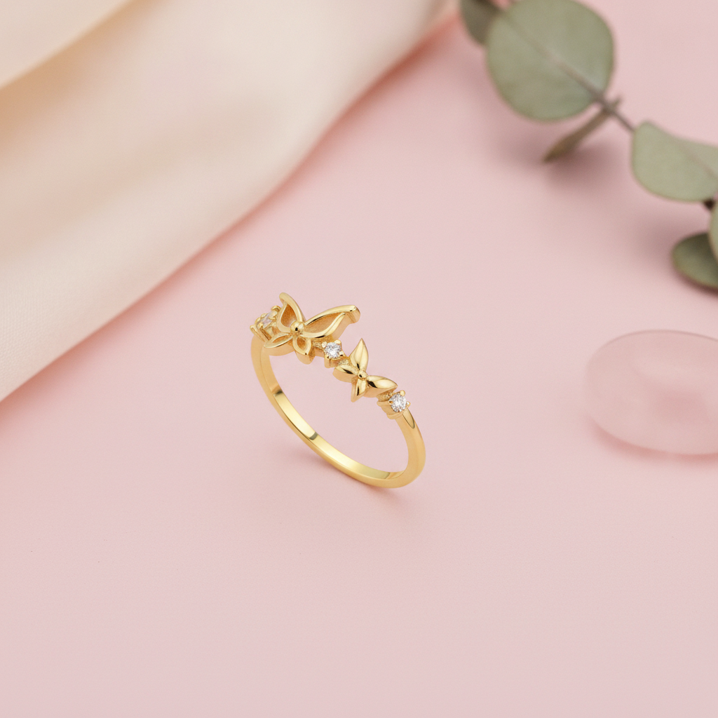gold ring with butterfly and flower motifs and clear stone accents displayed on pink background with eucalyptus leaves