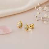 gold pear-shaped stud earrings paved with small stones and framed in beaded gold, on blush satin with a rose quartz stone and dried flowers