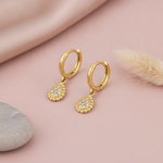gold huggie hoop earrings with a pave teardrop drop, on pink satin with a pebble and dried bunny tail grass