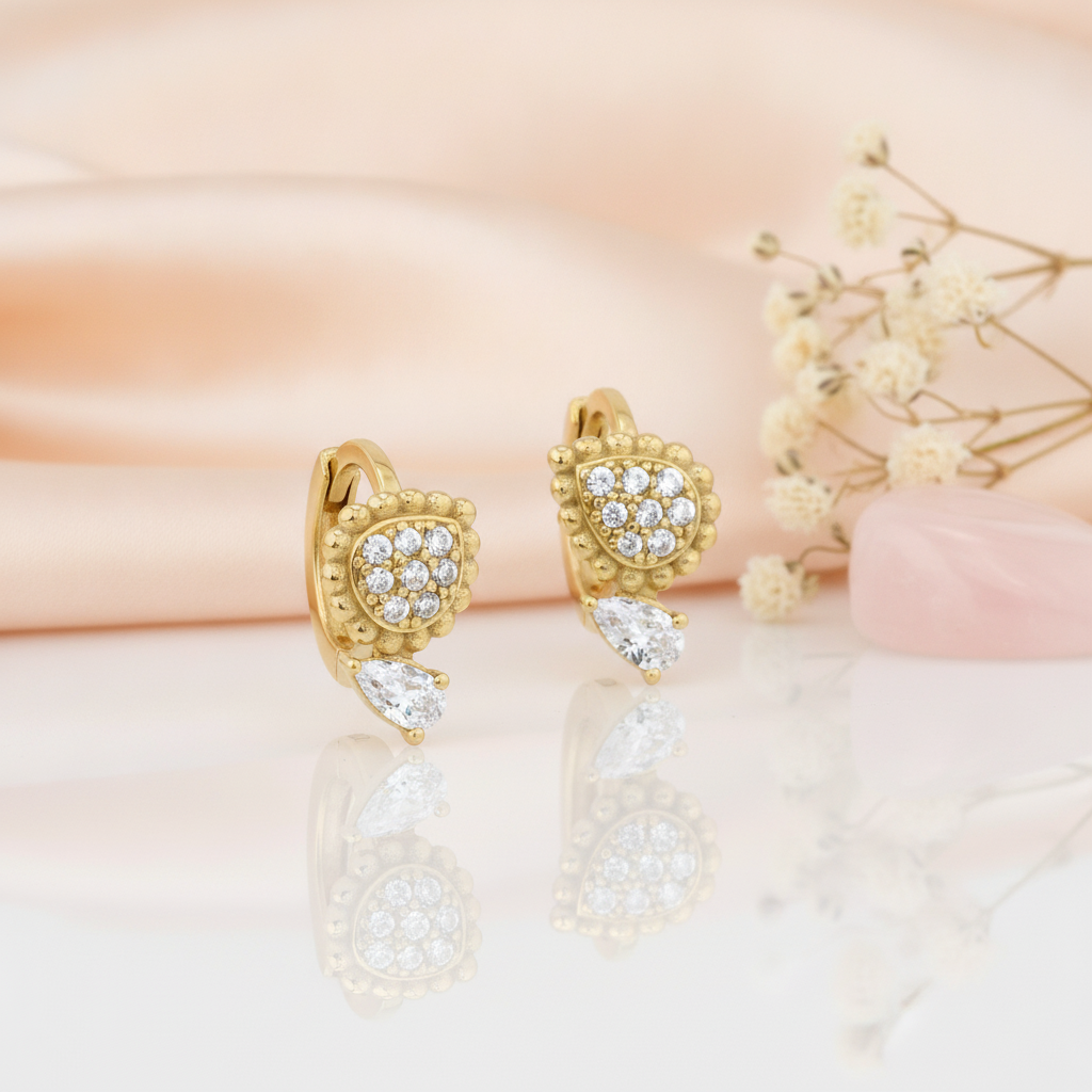 gold huggie hoop earrings with a beaded teardrop and a clear pear-cut stone drop, on peach satin with dried flowers and a rose quartz stone