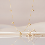 gold station necklace with five graduated pave teardrops on a fine chain, on cream satin with dried flowers