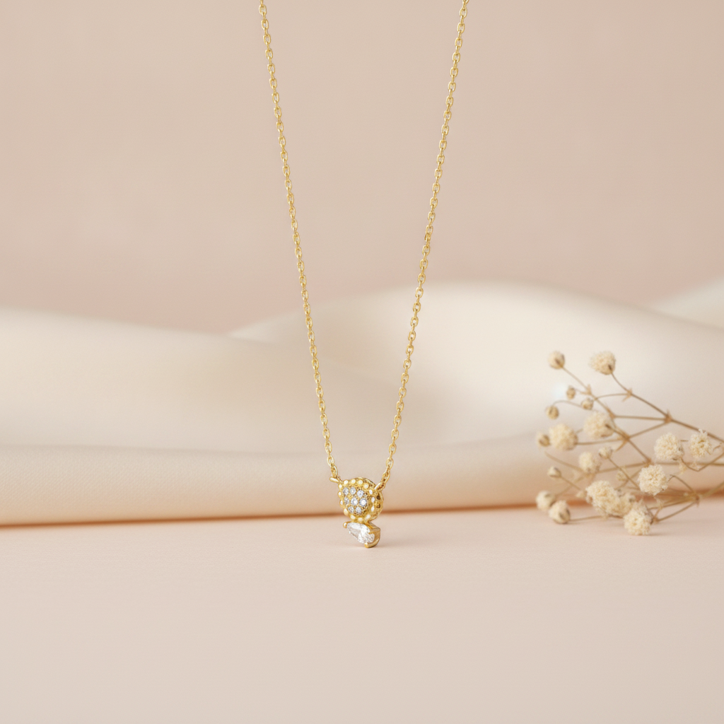 gold necklace with a beaded teardrop pendant and a clear pear-cut stone pendant side by side, on cream satin with dried flowers