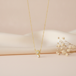 gold necklace with a beaded teardrop pendant and a clear pear-cut stone pendant side by side, on cream satin with dried flowers