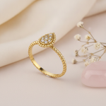 gold ring with a pave teardrop top on a twisted rope band, on cream satin with dried flowers and a rose quartz stone