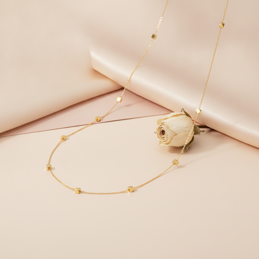 gold station necklace with faceted nuggets draped on blush fabric beside a dried cream rose