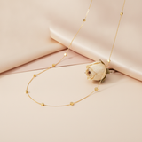 gold station necklace with faceted nuggets draped on blush fabric beside a dried cream rose