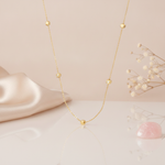 gold station necklace with faceted nuggets, a few set with small clear stones, hanging against a blush background with dried flowers